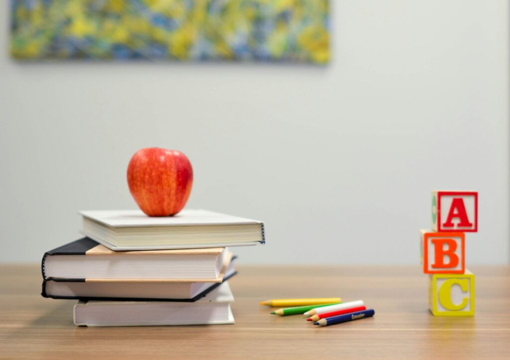 Teacher's desk with a pile of books and a red apple sitting at the top 

The Kristi Jones Podcast: How getting into the back to school mindset can help you in your personal growth 